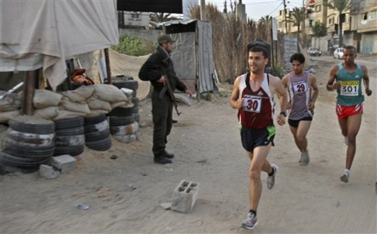 Palestinian Omar Abu Said, left, Azmi Majaideh, center, and Husam Naseir, right, participate in the first Gaza marathon, running past a Hamas security officer at a checkpoint in Beit Lahiya, northern Gaza Strip, on Thursday. 